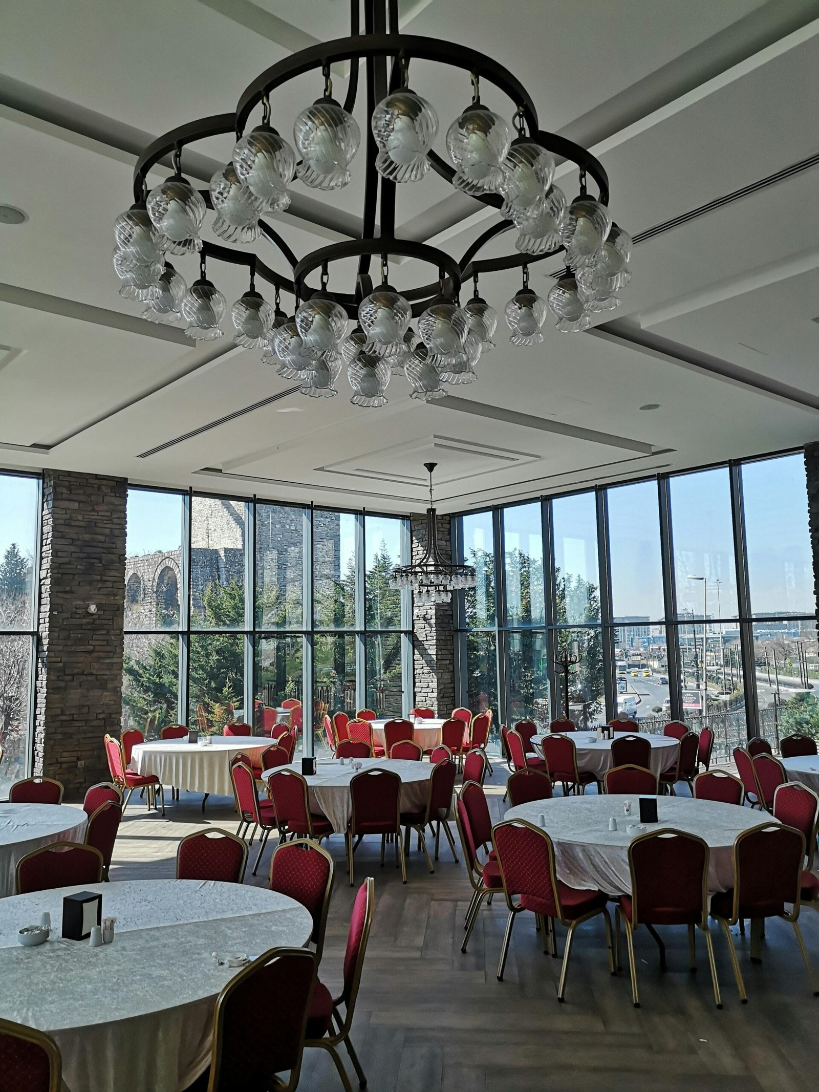 A spacious restaurant interior featuring a grand chandelier and large windows with a city view.